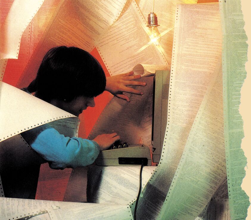 Junger Mann am Computer, umgeben von Endlospapier mit Programmlistings