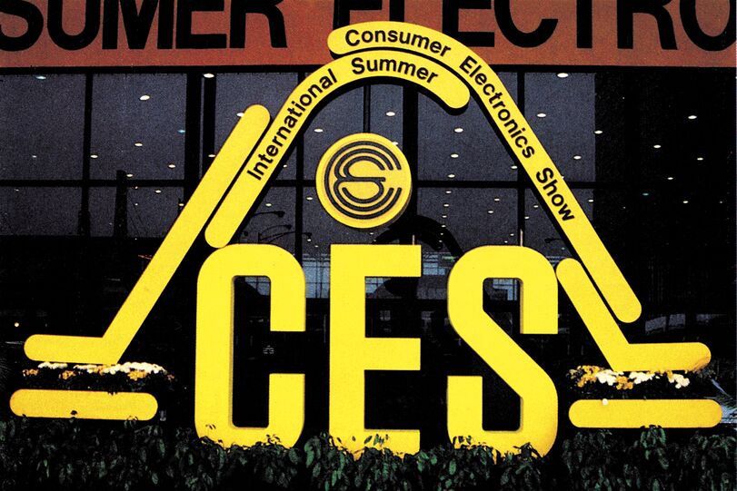 Großer gelber Aufsteller-Schriftzug »CES« mit Bogen »International Summer Consumer Electronics Show« vor einer Glasfassade bei Dämmerung