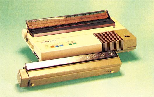 Beiger Matrixdrucker mit transparenter Abdeckhaube und farbigen Bedientasten, schräg von vorn