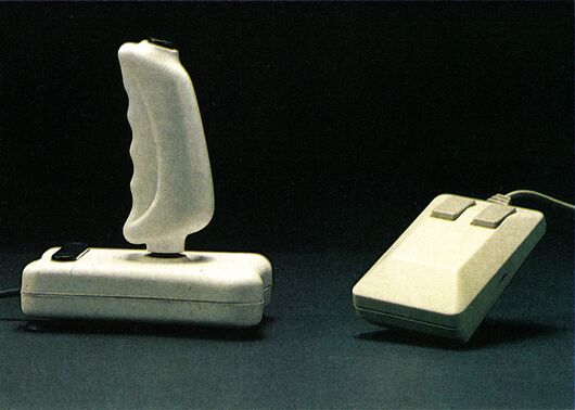 Farbfoto eines hellen Joysticks und einer Maus nebeneinander auf dunklem Grund
