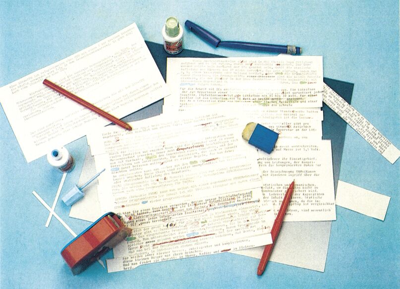 Farbfoto eines Schreibtischs mit handschriftlich korrigierten Manuskriptblättern, Stiften, Korrekturflüssigkeit und Radiergummi