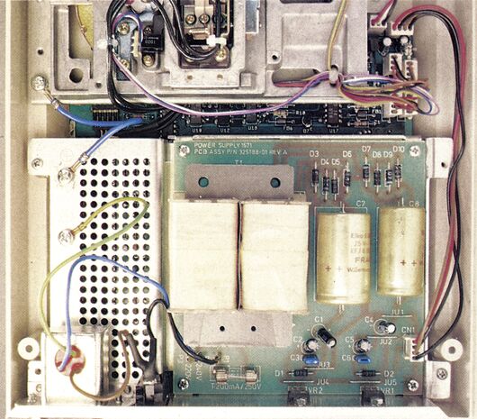 Farbfoto eines geöffneten Diskettenlaufwerks mit Netzteilplatine, Kondensatoren und farbiger Verkabelung