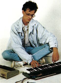 Foto einer Person, die im Schneidersitz vor einem Keyboard und einer Computertastatur sitzt