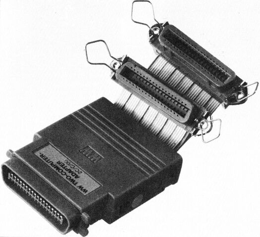Schwarzweißfoto eines Schnittstellen-Umschalters mit zwei Centronics-Steckern und Flachbandkabeln