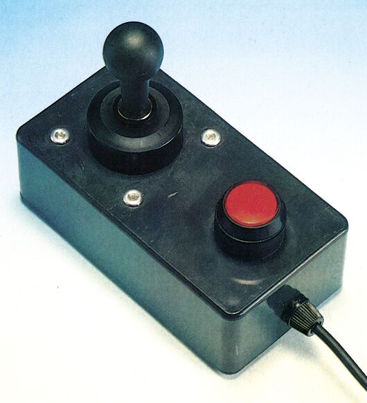 Joystick mit schwarzem Kugelgriff und großem rotem Feuerknopf auf hellem Grund