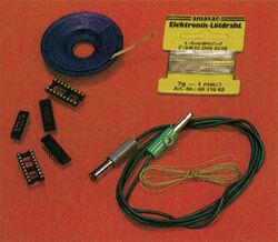 Auf rotem Grund: Rolle Entlötlitze, Päckchen Elektronik-Lötdraht, Chips, IC-Sockel und ein Kabel mit Stecker