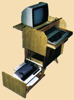 Computertisch aus hellem Holz mit Monitor, herausgezogener Tastaturablage und einem Drucker in einer ausgezogenen Schublade