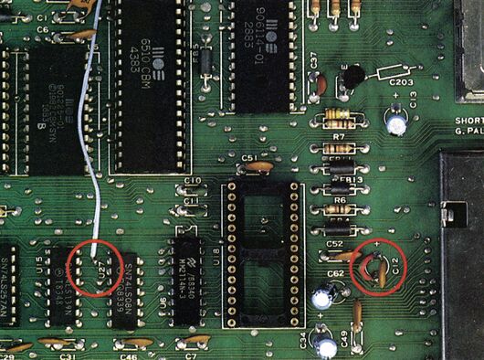 Ausschnitt einer grünen Computerplatine mit leerem IC-Sockel, daran ein angelöteter weißer Draht; zwei Stellen rot eingekreist