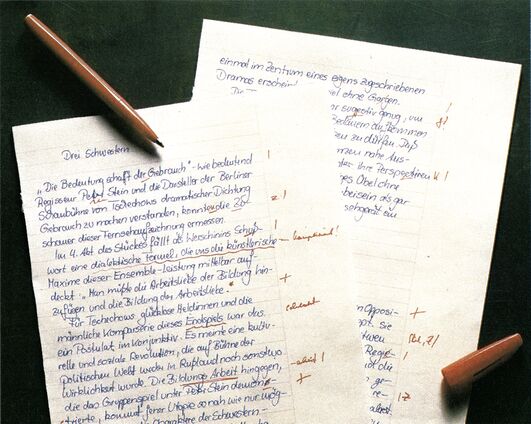 Handschriftlich beschriebene Blätter mit roten Korrekturzeichen, dazu zwei Stifte