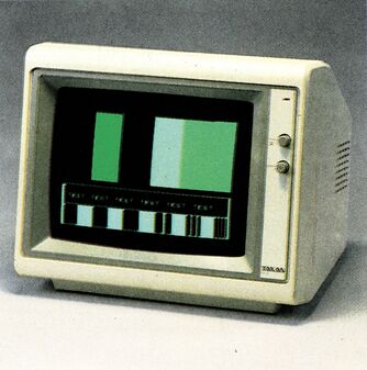 Monochromer Grünmonitor Taxan KX1201E im Dreiviertelprofil mit zwei Drehreglern rechts neben dem Bildschirm, auf dem Bildschirm ein Testbild in Grünstufen