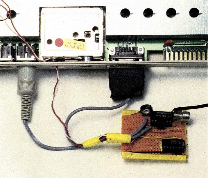 Farbfoto der Rückseite eines geöffneten Computers mit Anschlußbuchsen; davor eine Lochrasterplatine mit zwei ICs, Trimmpoti und Cinch-Buchse, verbunden über graue und gelbe Kabel