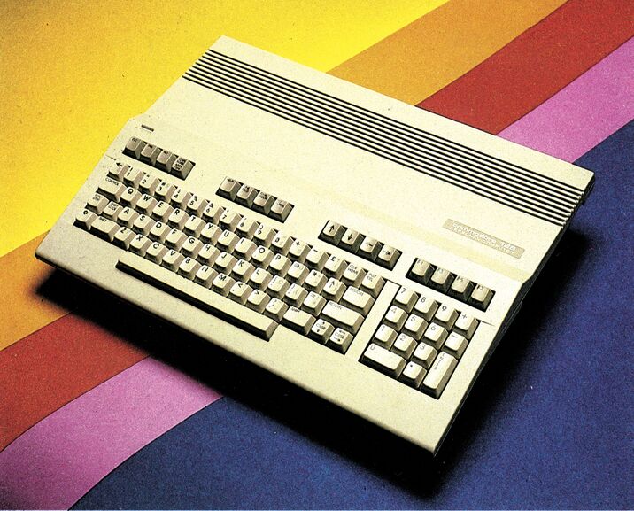 Farbfoto eines Commodore 128 mit integrierter Tastatur, schräg von oben vor einem Hintergrund aus diagonalen Farbstreifen in Gelb, Rot, Violett und Blau