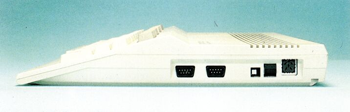 Farbfoto des C 128 von der Seite mit zwei neunpoligen Anschlüssen, einem Schiebeschalter und weiteren Öffnungen im Gehäuse