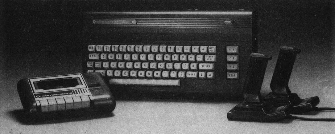 Foto: Computertastatur in dunklem Gehäuse, links davor eine Datasette, rechts zwei Joysticks